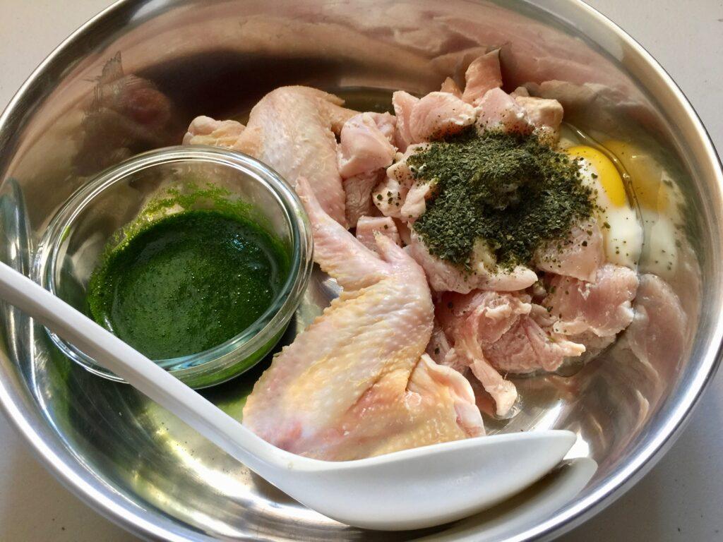 Dog bowl containing raw chicken wings, chicken breast, raw eggs, Norwegian sea kelp, and pureed spinach.